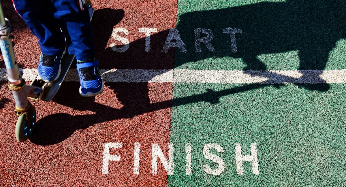 person on scooter crossing a start/finish line; large shadow