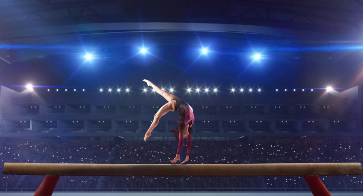 Female gymnast doing a complicated trick on gymnastics balance beam in a professional arena