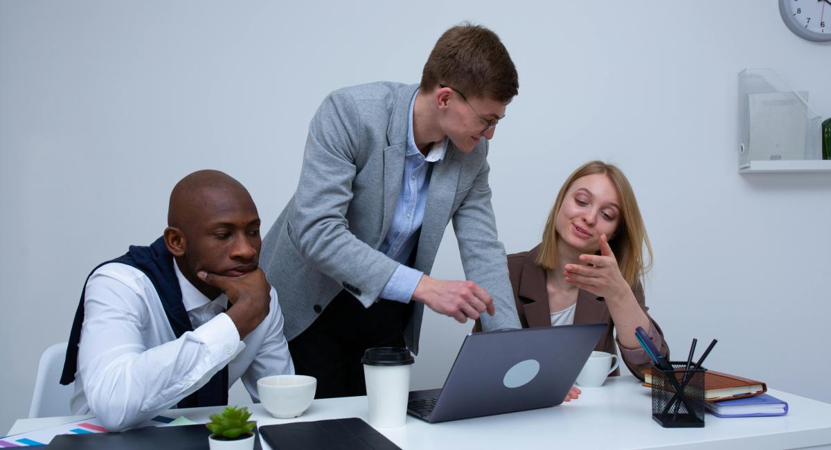 Group of business professionals in a meeting, discussing strategy around a laptop in a modern office setting.