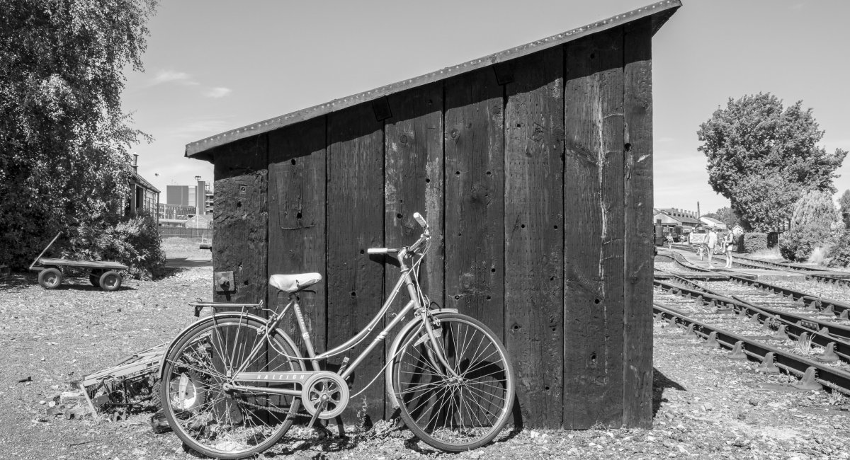 Black-and-white photo of bike leaning up against small shed