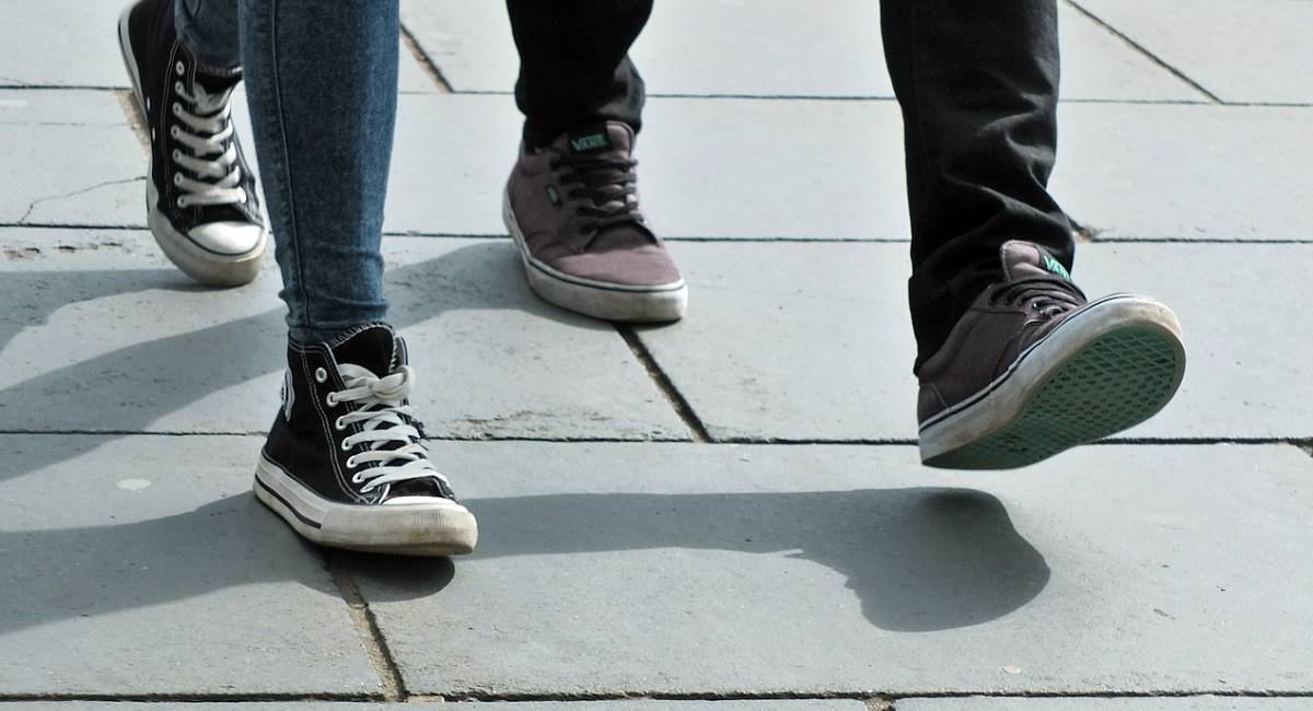 The feet of two people walking together, wearing sneakers