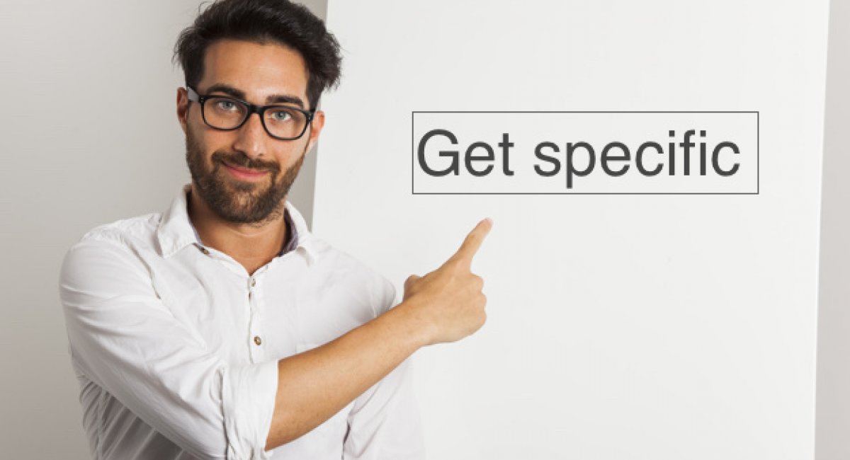 Man pointing to words on wall, "Get specific"